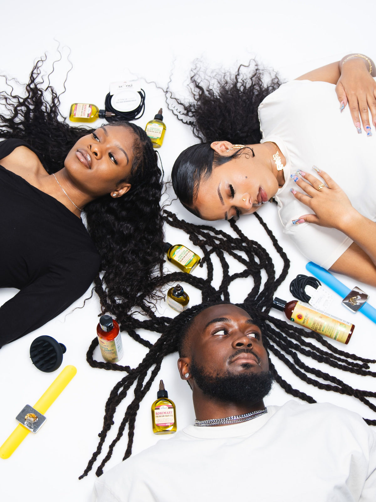 Three people with styled hair lying on a white surface surrounded by hair care products.