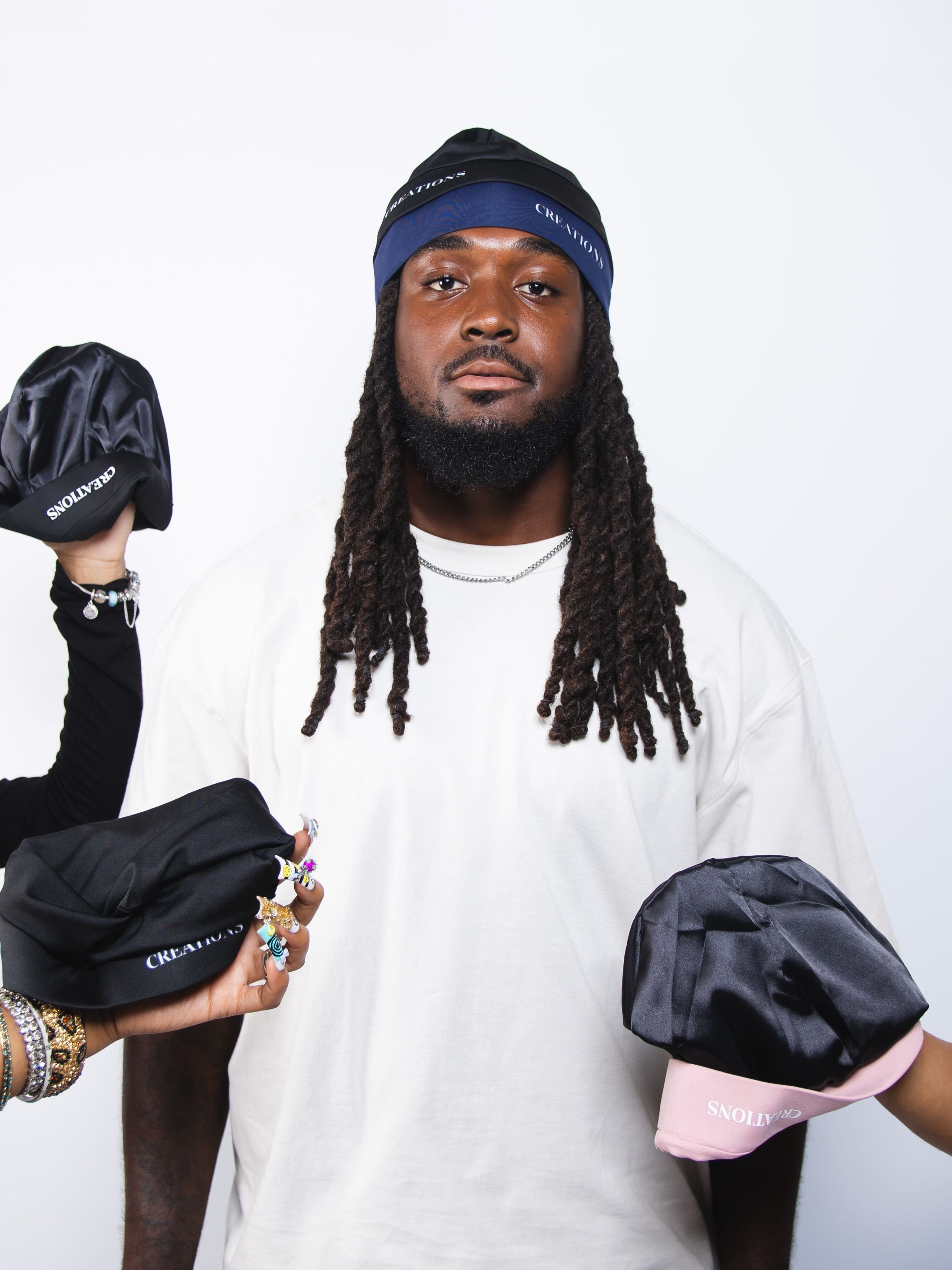 Person holding black satin skull caps with visible branding against a white background