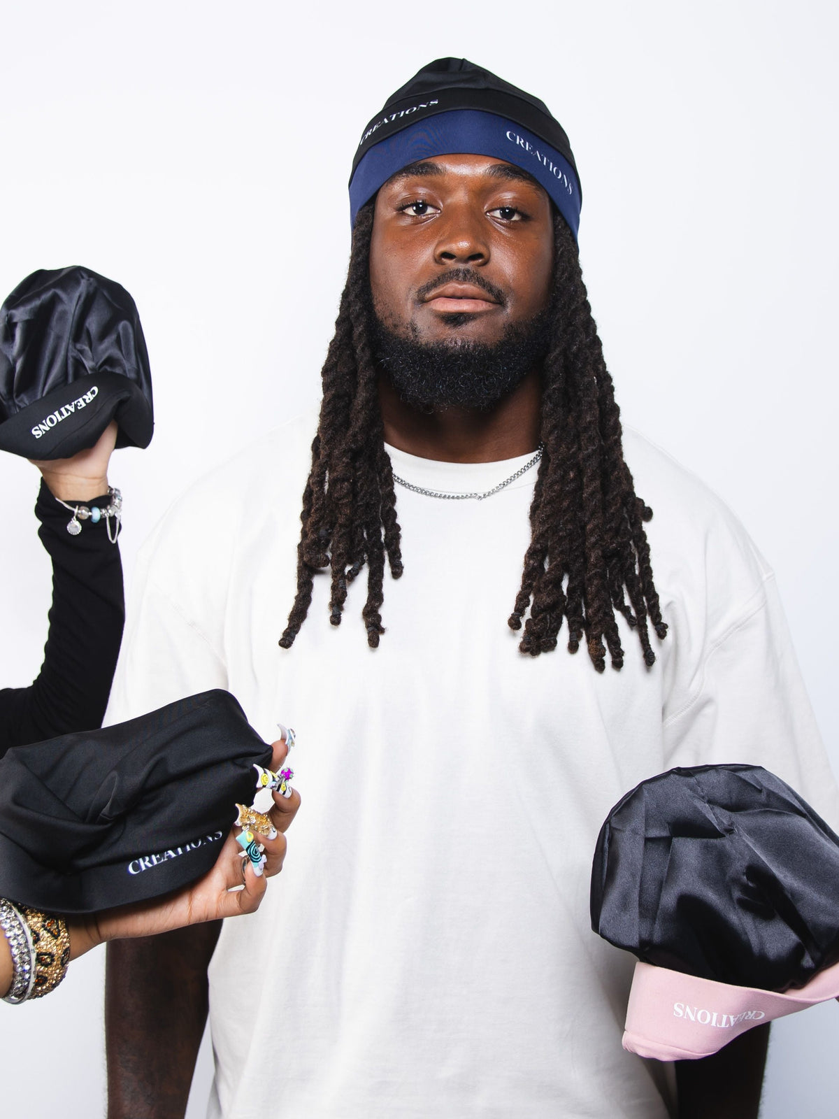 Person holding black satin skull caps with visible branding against a white background
